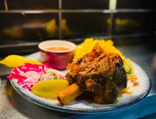 Mahiche lamb shank on a plate with saffron rice, lemon, and pickled red cabbage in Soofi Restaurant.